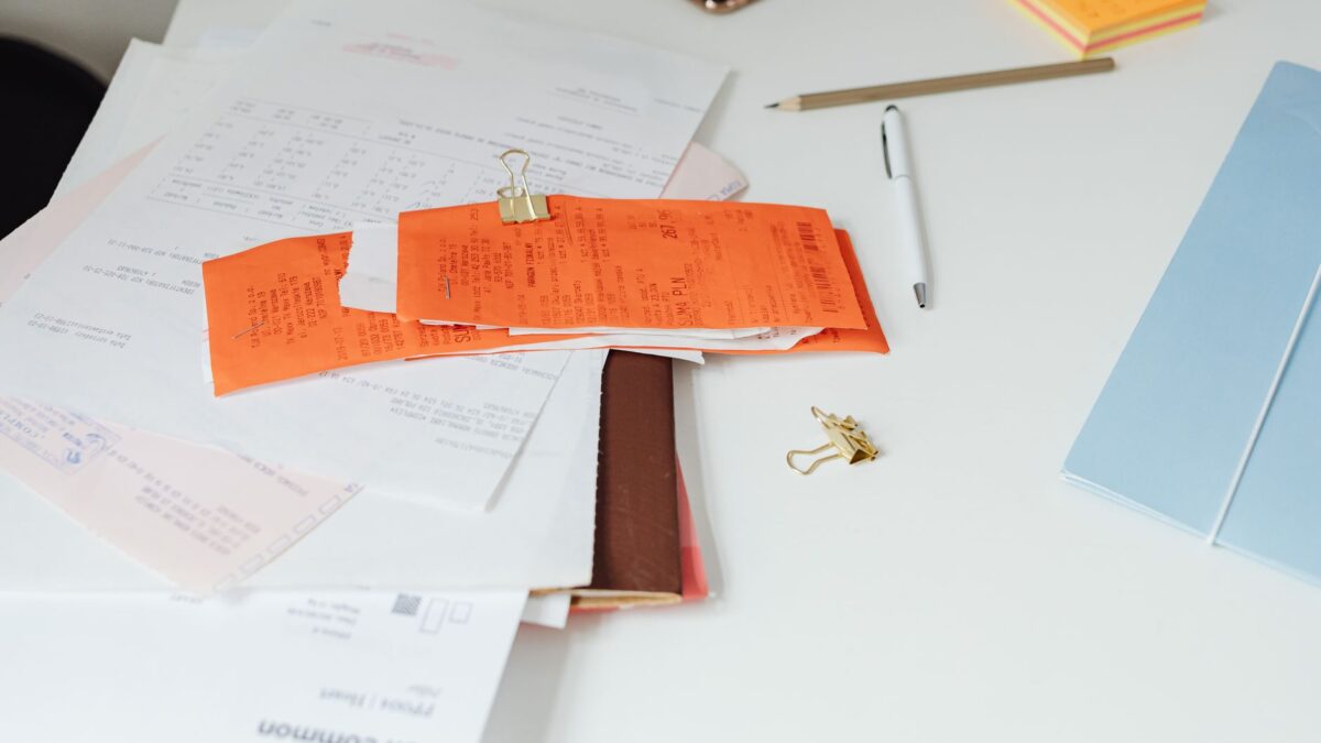 Schreibtisch mit Rechnungen, Notizblock und Laptop einer selbstständig arbeitenden Person